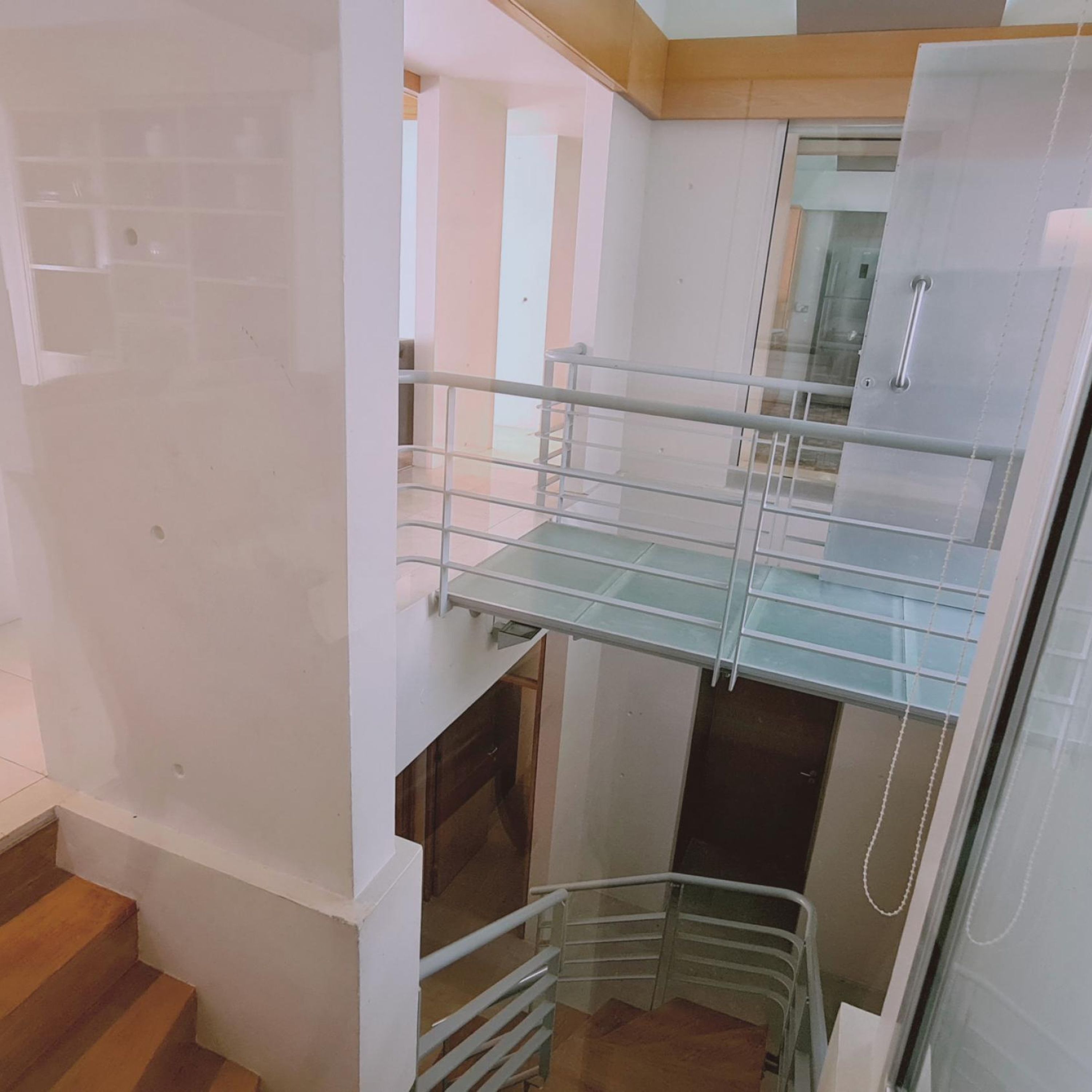 Un interior de varios niveles con barandilla de cristal, escalones de madera y pasamanos de metal.