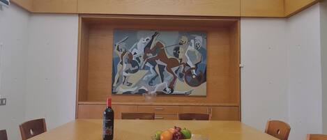 A conference room with a large table, chairs, a painting on the wall, and a bottle of wine on the table.