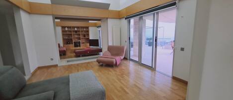 Un amplio espacio de sala con un gran ventanal corredera que da a un balcón exterior.