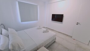 Un dormitorio moderno y minimalista con una cama grande, un televisor montado en la pared y una puerta con picaporte.