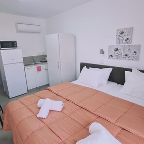 Una camera da letto con un letto, cuscini bianchi, un piumone color pesca, un asciugamano bianco, un forno a microonde, un frigorifero, un lavandino e un armadietto.