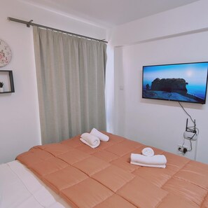 Una camera da letto con un letto, una televisione montata a parete e una finestra con tende.