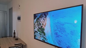 A room with a large flat-screen TV mounted on the wall displaying a coastal scene. - 100 AN - Napa Living 23 (Ayia Napa)