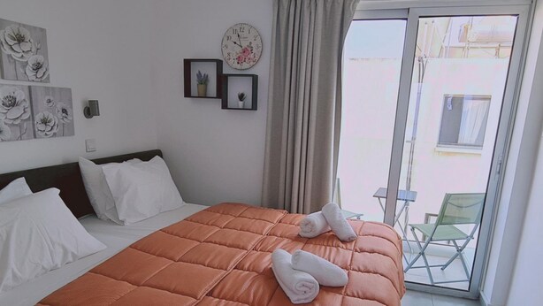 A hotel room with a large bed, a view of the outside, and a clock on the wall. - 100 AN - Napa Living 23 (Ayia Napa)