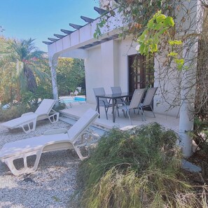A covered outdoor seating area with lounge chairs and a table, a pool, and surrounding vegetation. - 22 PSR - Stay Villa Michalis (Pissouri)