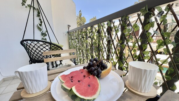 A table with a plate of watermelon slices and grapes, two white cups, and a hanging chair. - 91 KPF - Stay Artifex Apartment (Paphos)