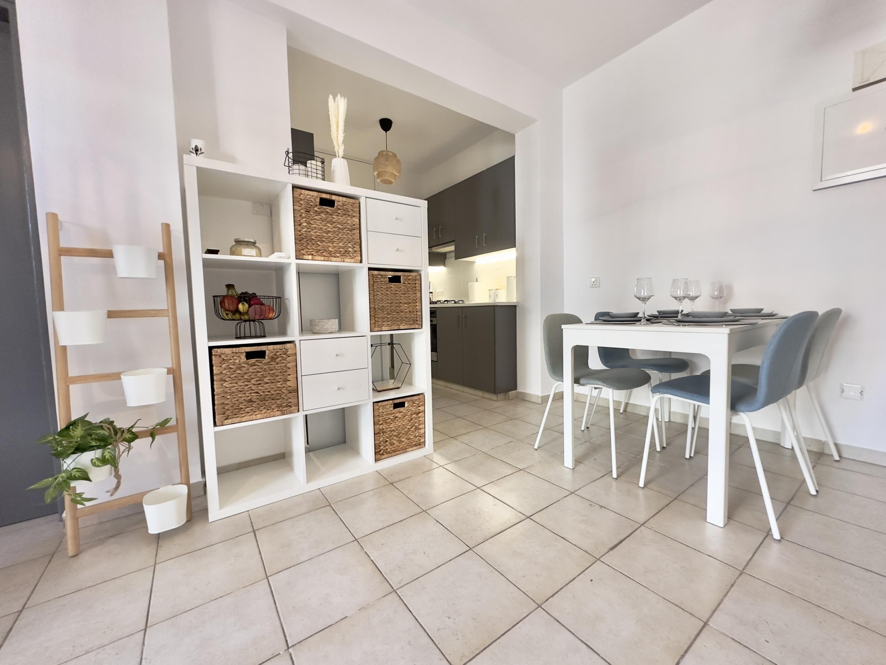 Una cucina moderna con mobili bianchi, un tavolo da pranzo con sedie e un mobile contenitore a parete con cesti.