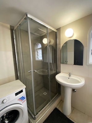 A bathroom with a glass-enclosed shower, a sink, and a washing machine.