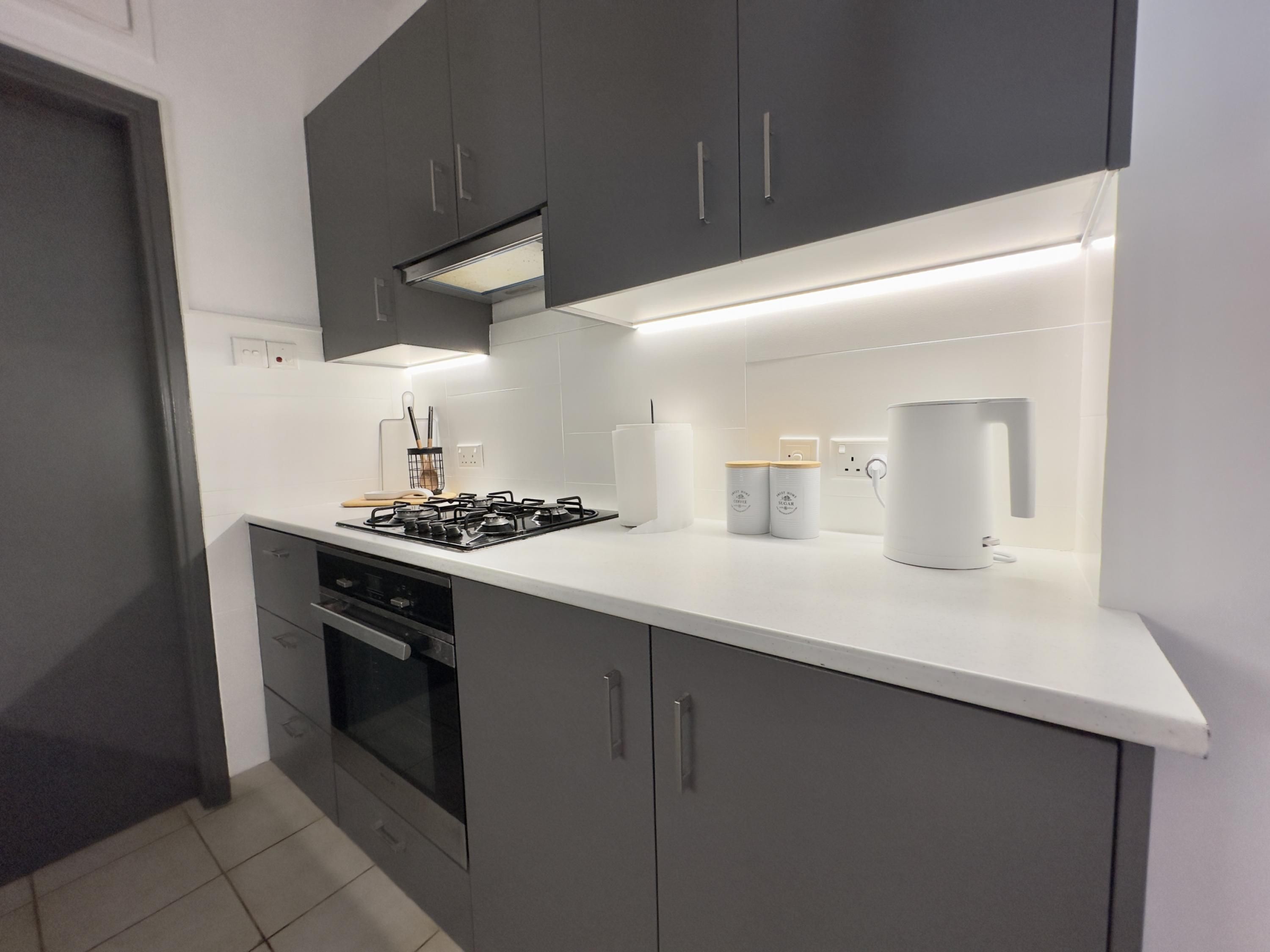 A modern kitchen with grey cabinets, a white countertop, a gas stove, an oven, and a coffee machine.
