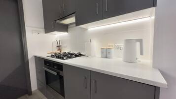 A modern kitchen with grey cabinets, a white countertop, a gas stove, an oven, and a coffee machine.
