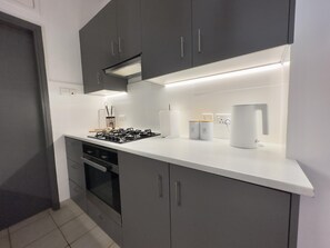 A modern kitchen with grey cabinets, a white countertop, a gas stove, an oven, and a coffee machine.