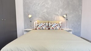 A bedroom with a large bed, two bedside lamps, a grey wardrobe, and a textured wall. - 91 KPF - Stay Artifex Apartment (Paphos)