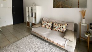 A modern living room with a sofa, a large rug, and two wicker pendant lights. - 91 KPF - Stay Artifex Apartment (Paphos)