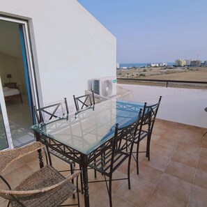 A glass-top table with chairs on a balcony with a view of the beach and buildings. - 69 LCA - Stay Sea and Salt Lake Panoramic View Apt (Larnaca)