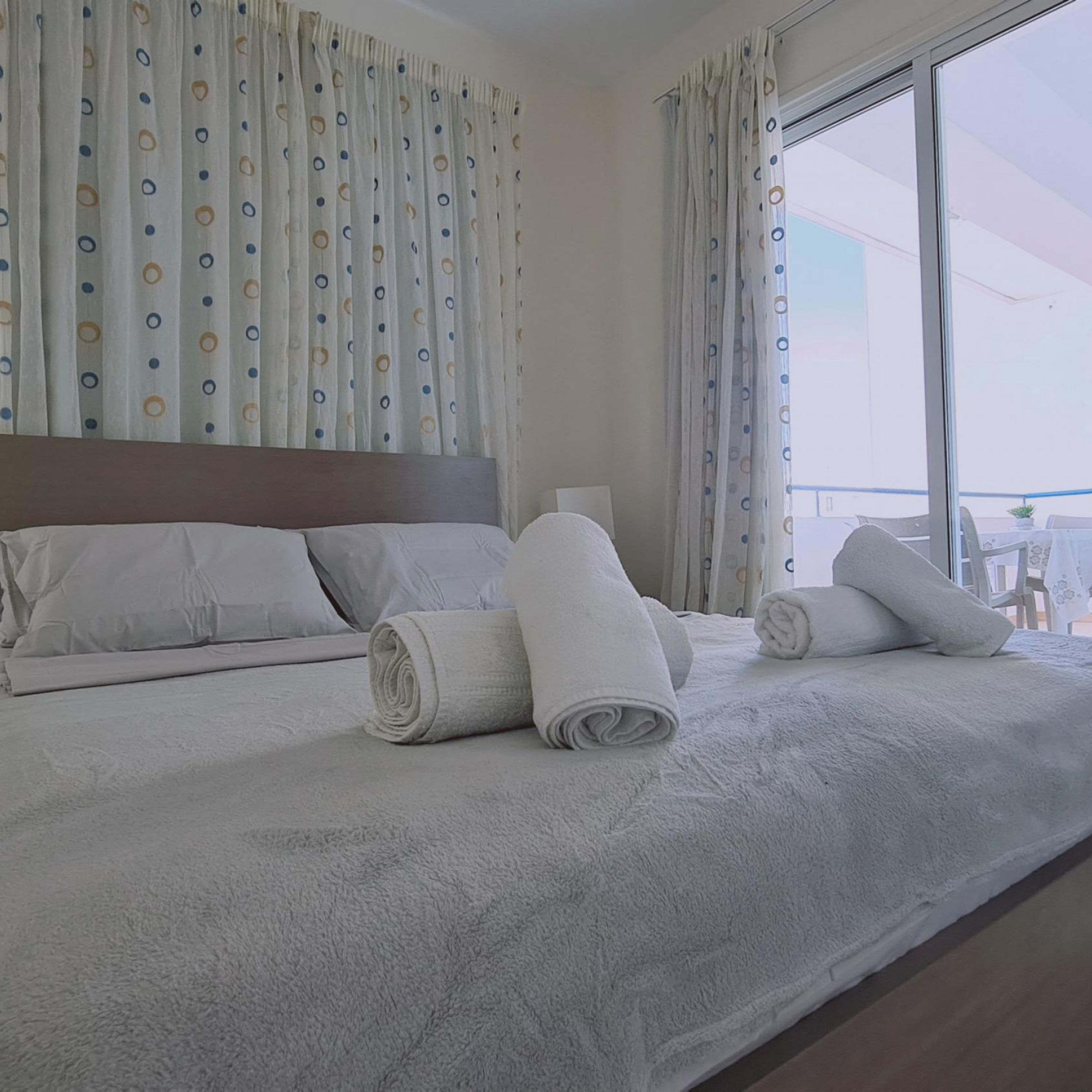 A neatly made bed with white linens, a headboard, and rolled towels.