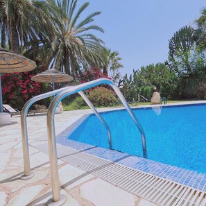 Une piscine avec un escalier en métal, des chaises longues et des palmiers en arrière-plan.