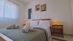 A hotel room with a bed, two bedside lamps, a window with sheer curtains, and two wall-mounted flower paintings. - 90 TLA - Stay Tala Sea View Apartment (Tala)