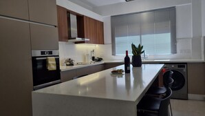 A modern kitchen with a central island, built-in oven, and a washing machine. - 97 LIM - Stay Vital Elegance Apartment (Limassol)