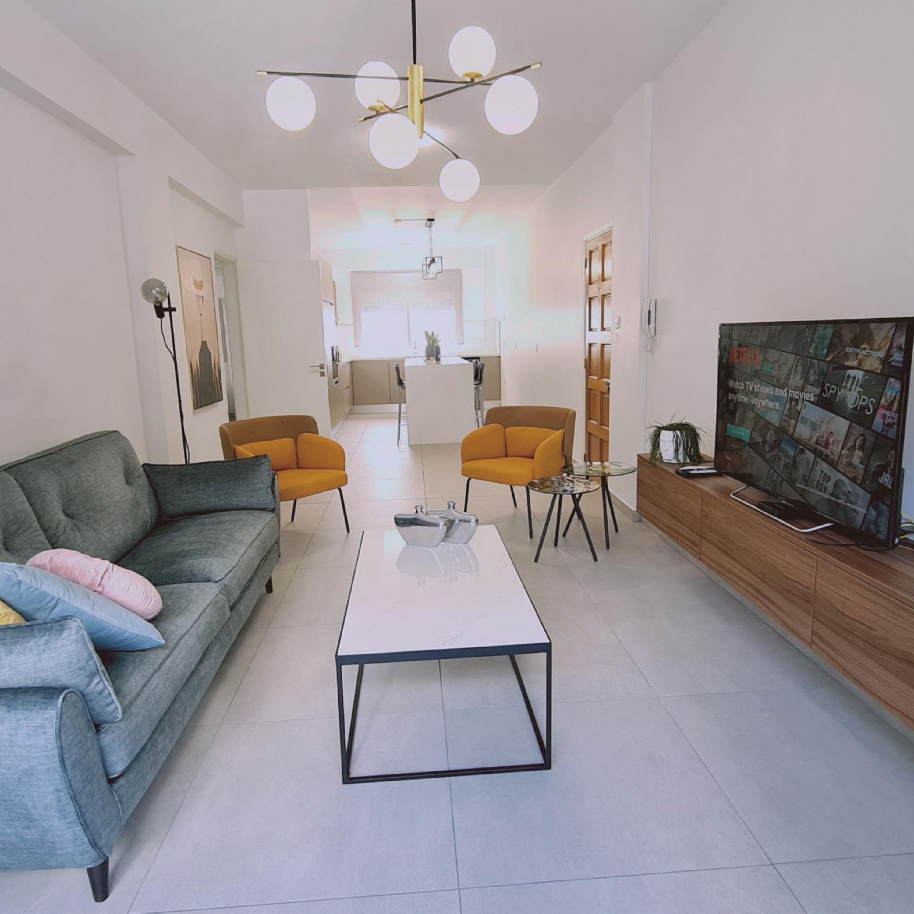Een moderne woonkamer met een grijze bank, twee oranje fauteuils, een witte salontafel en een televisie op een houten kast.