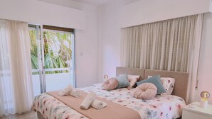 A bedroom with a bed, a nightstand, a window with curtains, and a view of greenery outside. - 97 LIM - Stay Vital Elegance Apartment (Limassol)