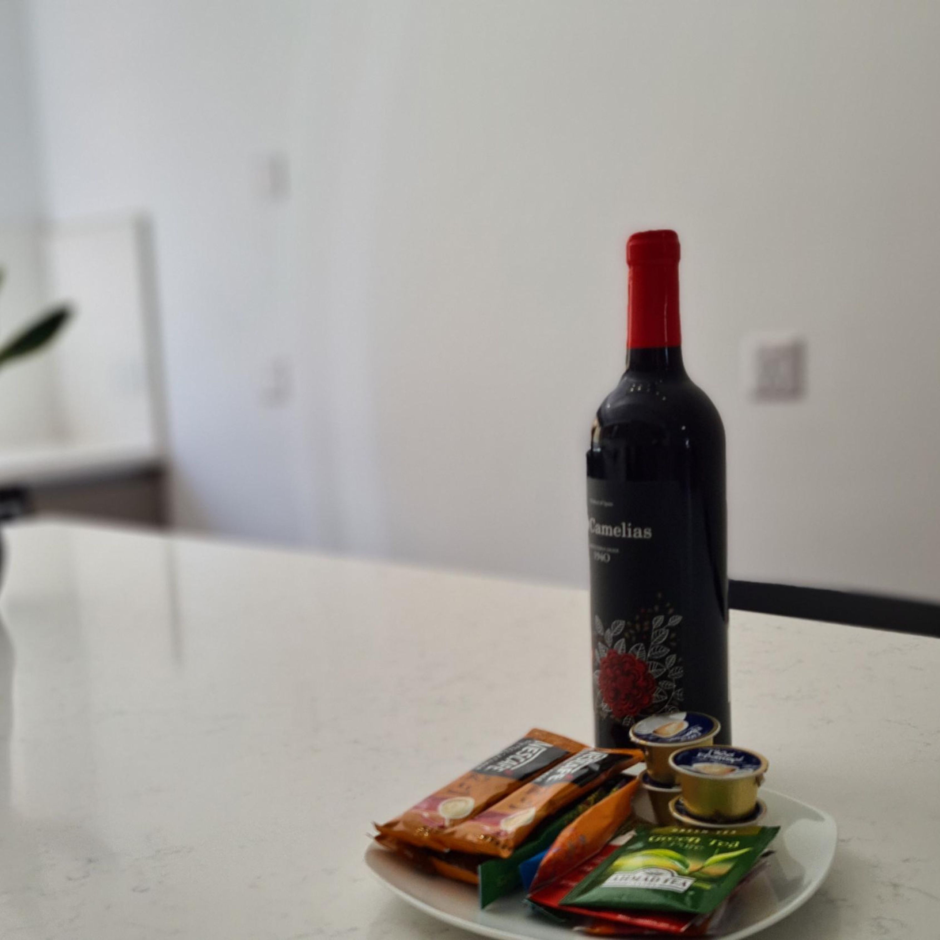 A bottle of wine, a plate with snacks, and a small bowl on a white countertop.