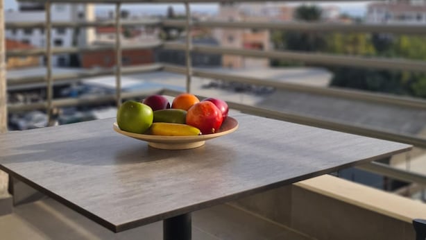 Une table avec un saladier de fruits sur un balcon donnant sur une vue panoramique de la ville.