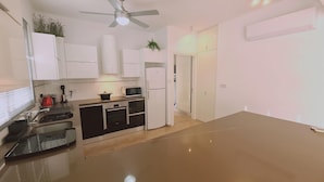 Une cuisine moderne avec des meubles blancs, un four à micro-ondes, une cuisinière et un ventilateur de plafond.