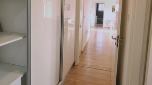 Un couloir au plancher de bois mène à une pièce où se trouvent un lit et un bureau.