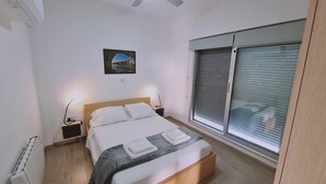 Une chambre à coucher comprenant un lit, deux tables de chevet, une lampe de chevet, une fenêtre avec des stores et un tableau accroché au mur.