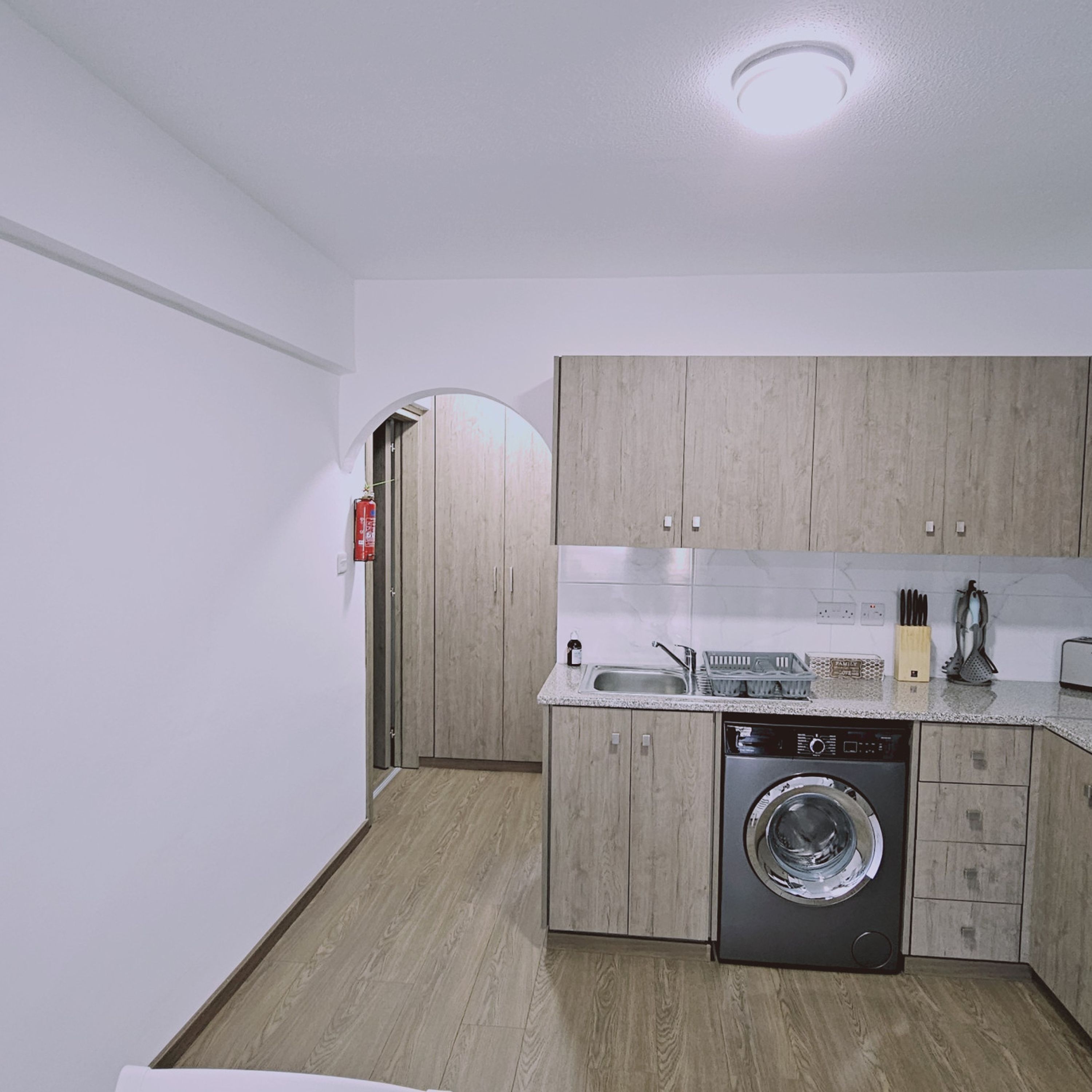 Una cocina funcional con armarios de madera, lavadora y pileta.