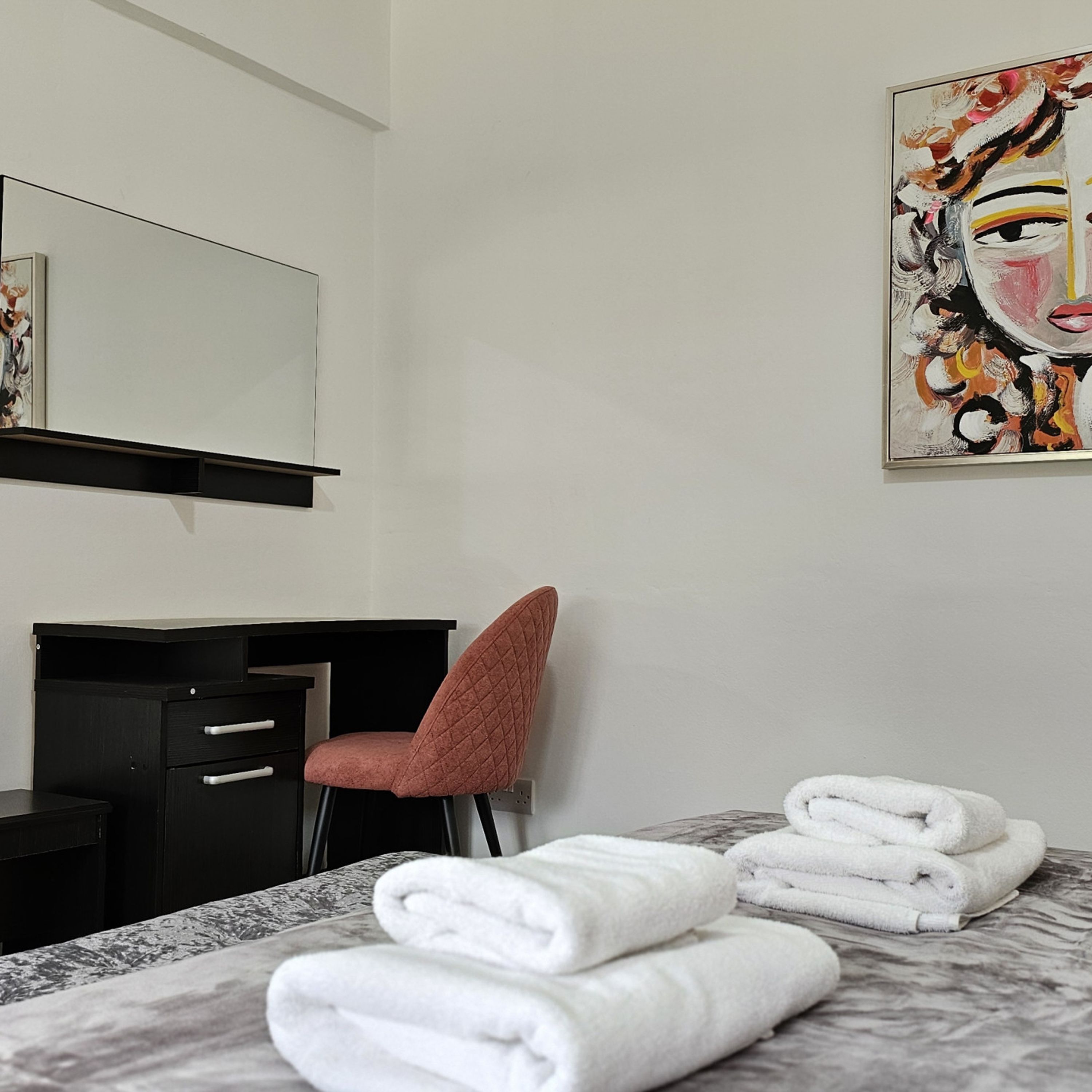 A hotel room with a bed, a desk, a chair, and a painting on the wall.