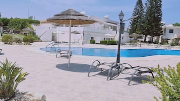 Zona de piscina con sillones de descanso y una sombrilla de paja.