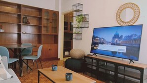 Ein Wohnzimmer mit Holzboden, einem Fernseher auf einem Schrank, einer Couch, einem Couchtisch und einem Bücherregal.