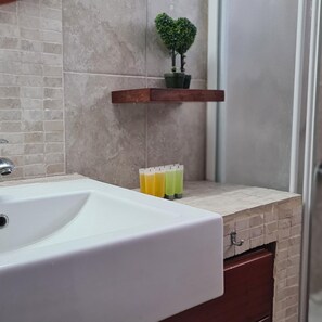 A bathroom with a white sink, a heart-shaped plant on a shelf, and a row of colorful bottles. - 19 LCA - Stay Antique Apartment (Larnaca)