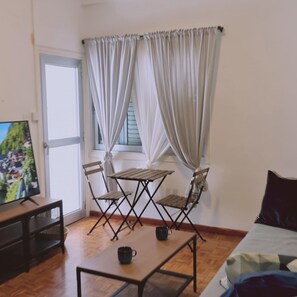 A room with a wooden table and chairs, a TV on a stand, and a window with curtains. - 19 LCA - Stay Antique Apartment (Larnaca)