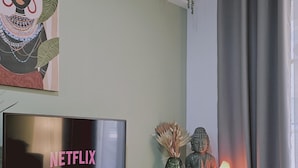 A living room with a TV displaying 'NETFLIX', a Buddha statue, and a small table with decorative items. - 103 LCA - Stay Green Apartment (Larnaca)