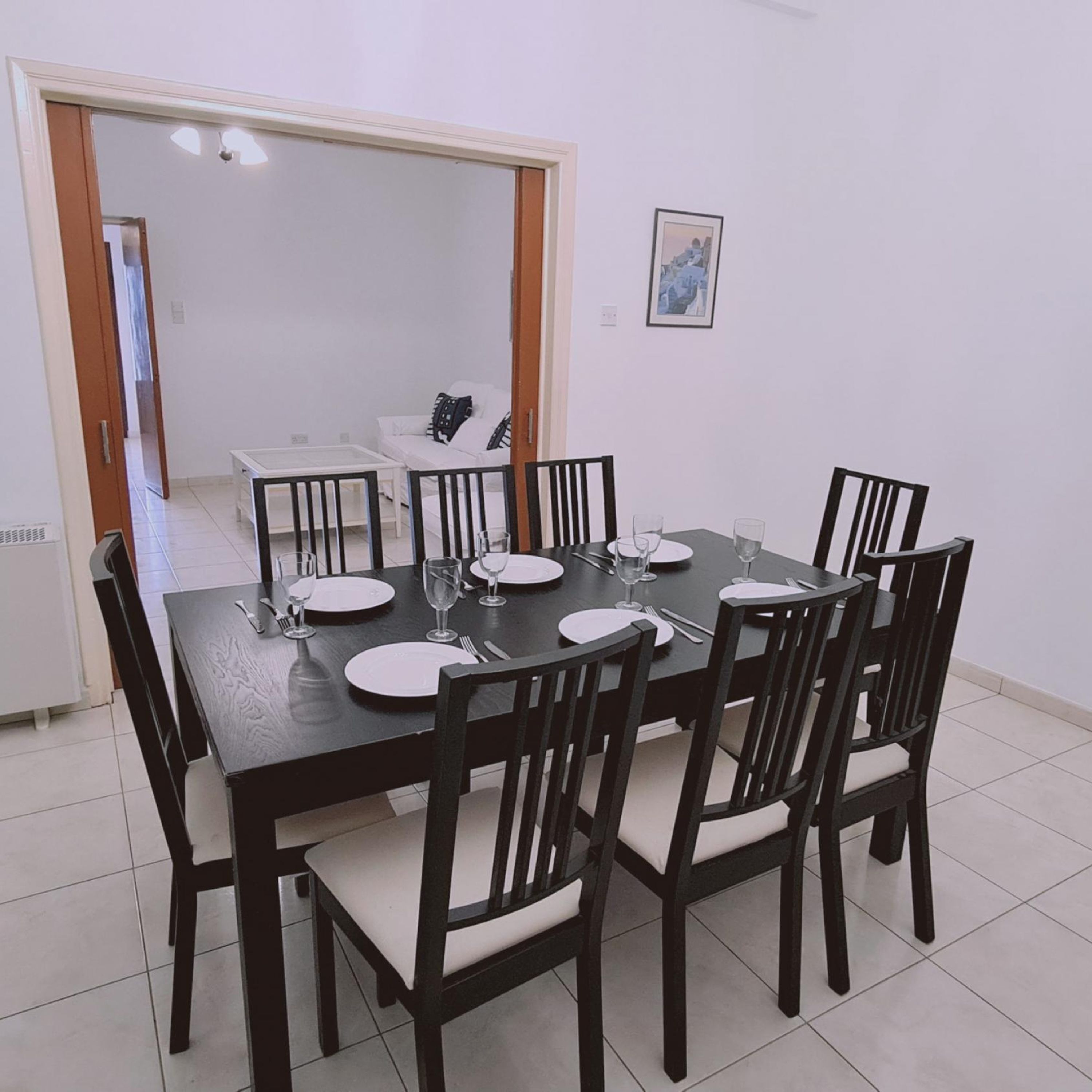 Uma área de refeições com uma mesa retangular posta para seis pessoas, rodeada por seis cadeiras com assentos acolchoados.