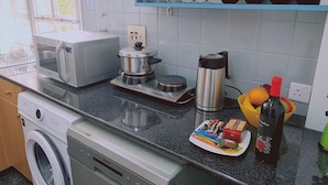 A kitchen with a washing machine, microwave, coffee maker, and a plate of snacks. - 57 NIC - Stay Chrysanthemum City Apartment (Nicosia)