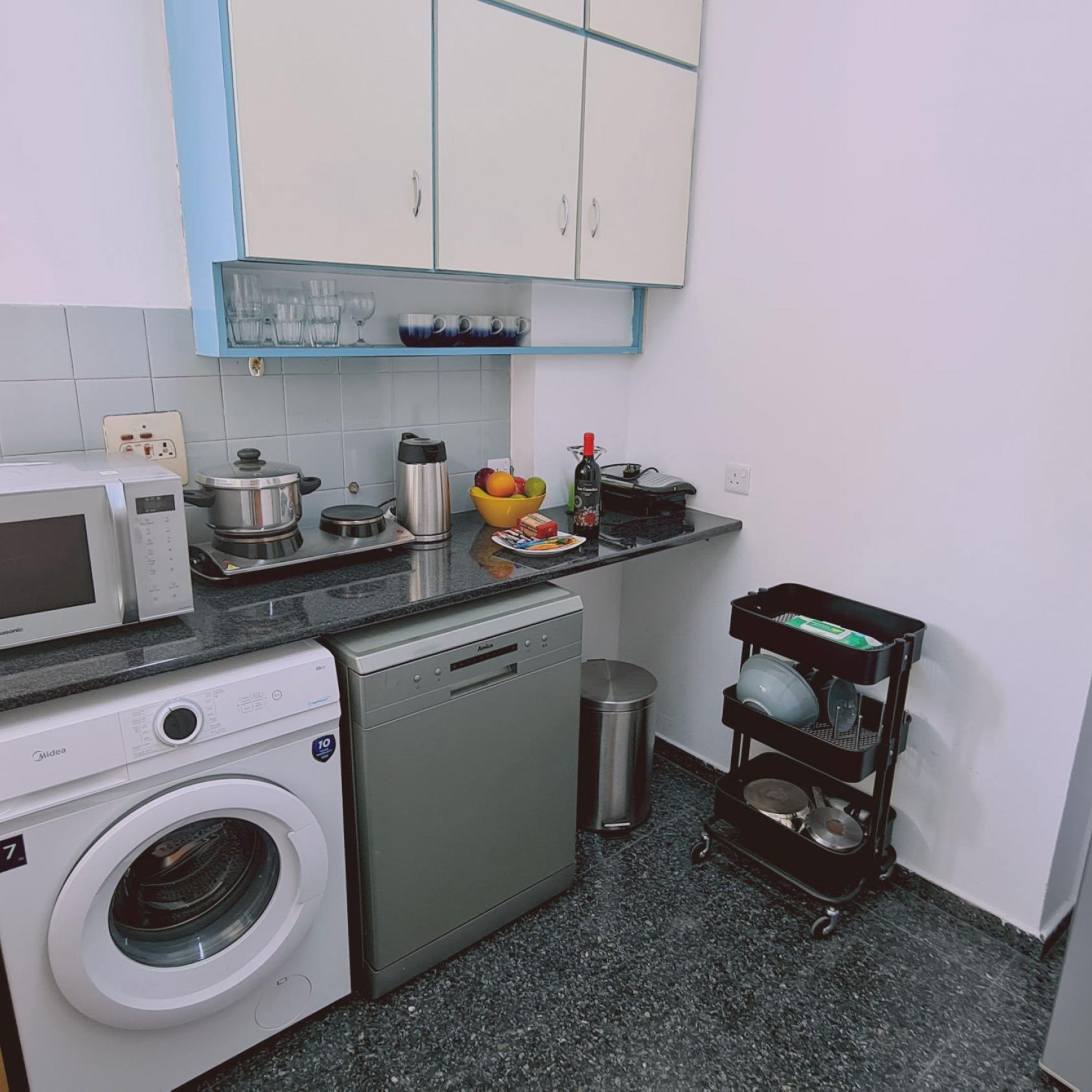A compact kitchen with a washing machine, dishwasher, microwave, and a small trash bin.
