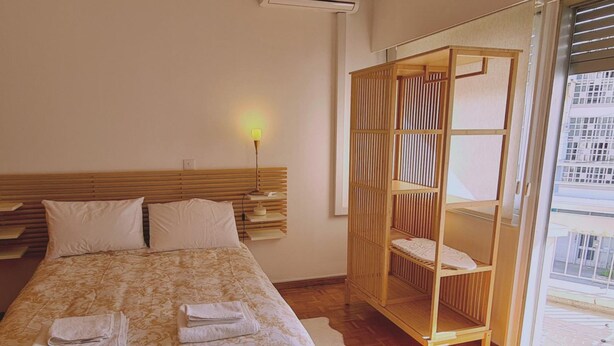 A hotel room with a bed, bedside table, lamp, and a view of the city through a large window. - 57 NIC - Stay Chrysanthemum City Apartment (Nicosia)