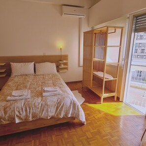 A hotel room with a bed, bedside table, lamp, and a view of the city through a large window. - 57 NIC - Stay Chrysanthemum City Apartment (Nicosia)
