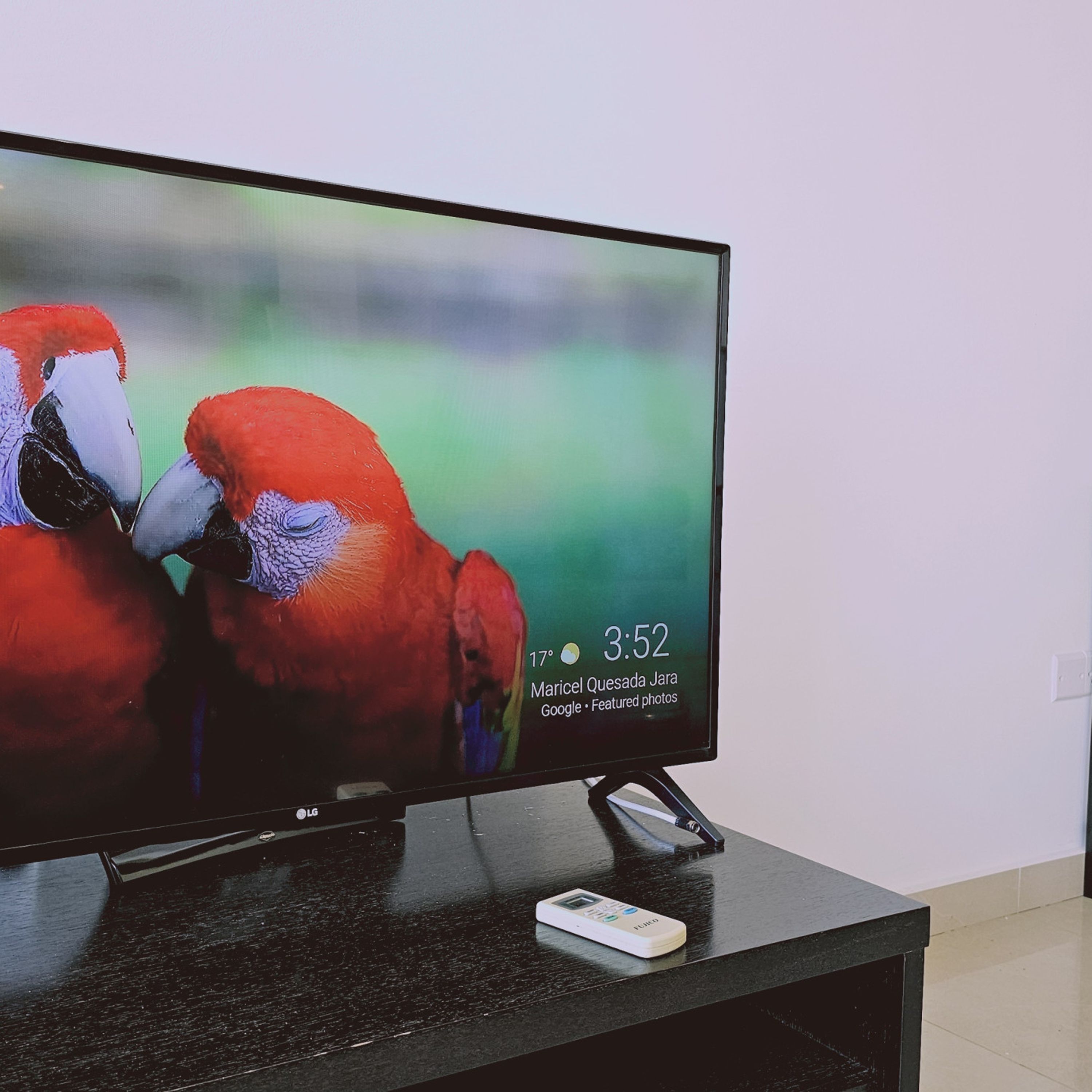 A flat-screen TV on a black stand with a remote control beside it.