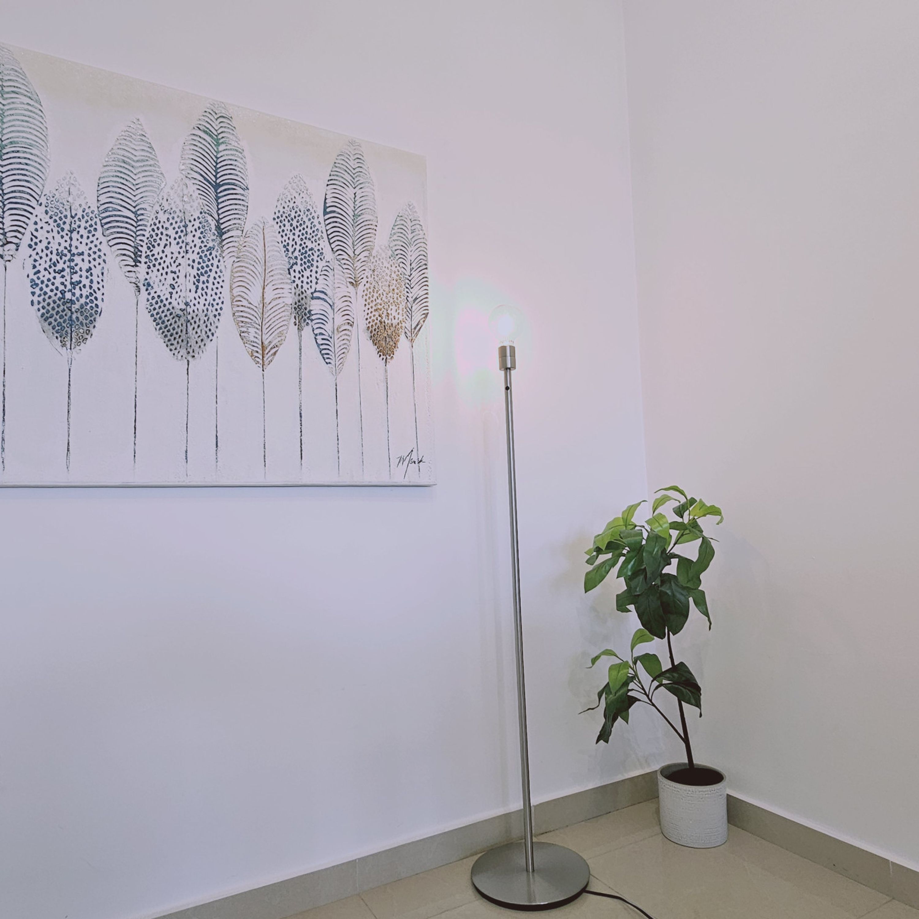 A room with a floor lamp, a potted plant, and a wall-mounted artwork.