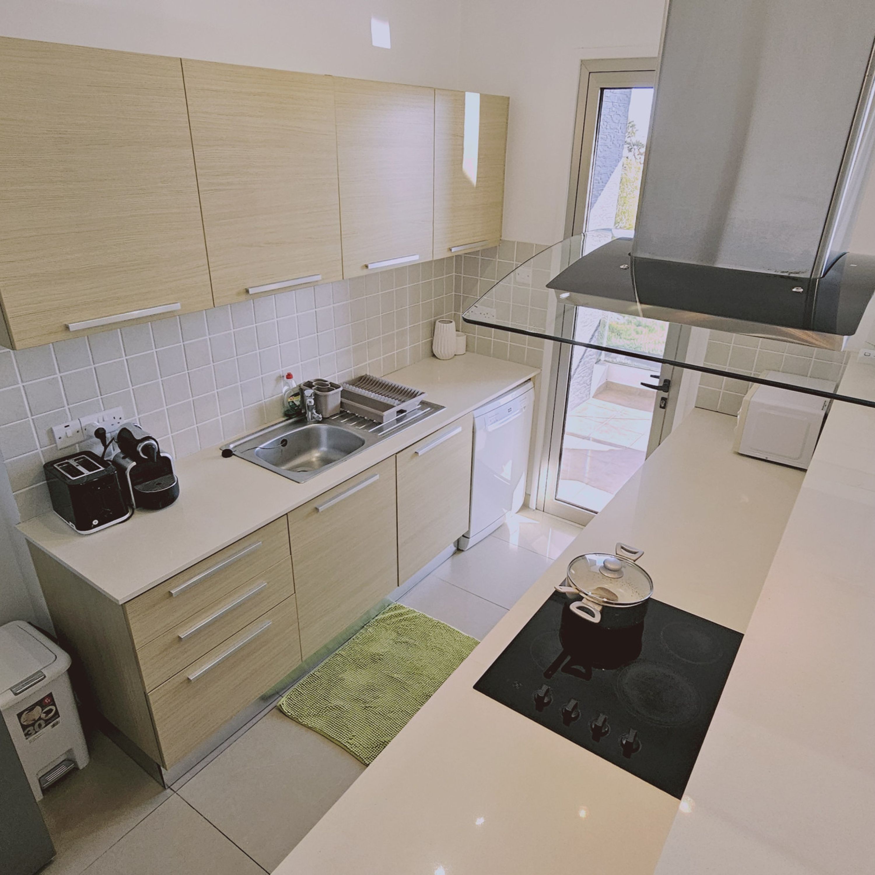 A modern kitchen with light wood cabinets, a stainless steel sink, a glass backsplash, and a black stove.