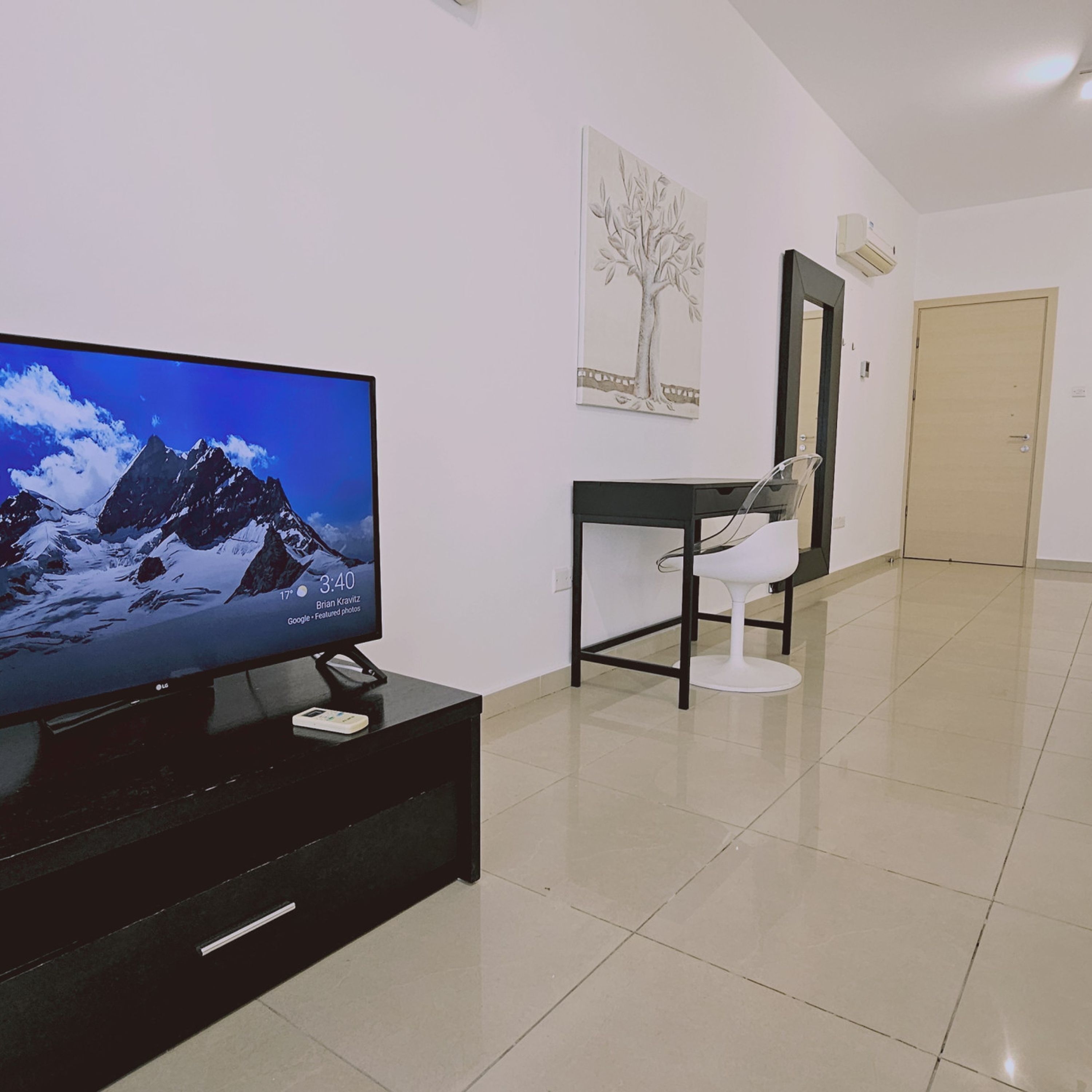 Ein modernes Wohnzimmer mit einem Flachbildfernseher auf einem schwarzen Standfuß, einem weißen Sessel, einem schwarzen Tisch und einer Tür im Hintergrund.