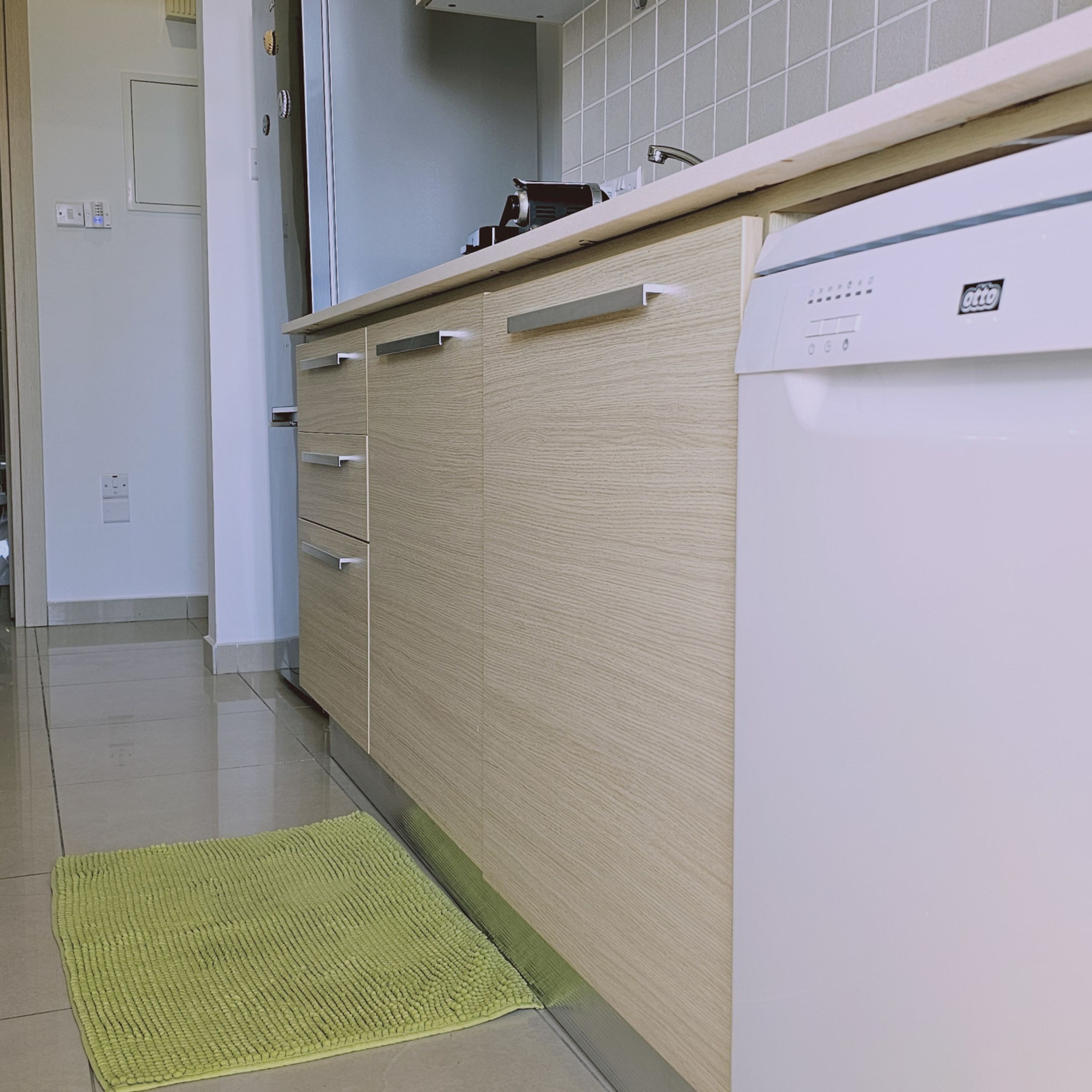 A kitchen with a wooden cabinet, a white dishwasher, and a green mat on the floor.