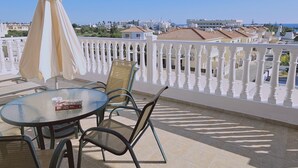 A terrace with a table and chairs, a white balustrade, and a view of the city and sea. - 116 AN - Stay Nissi Blossom Apartment (Ayia Napa)