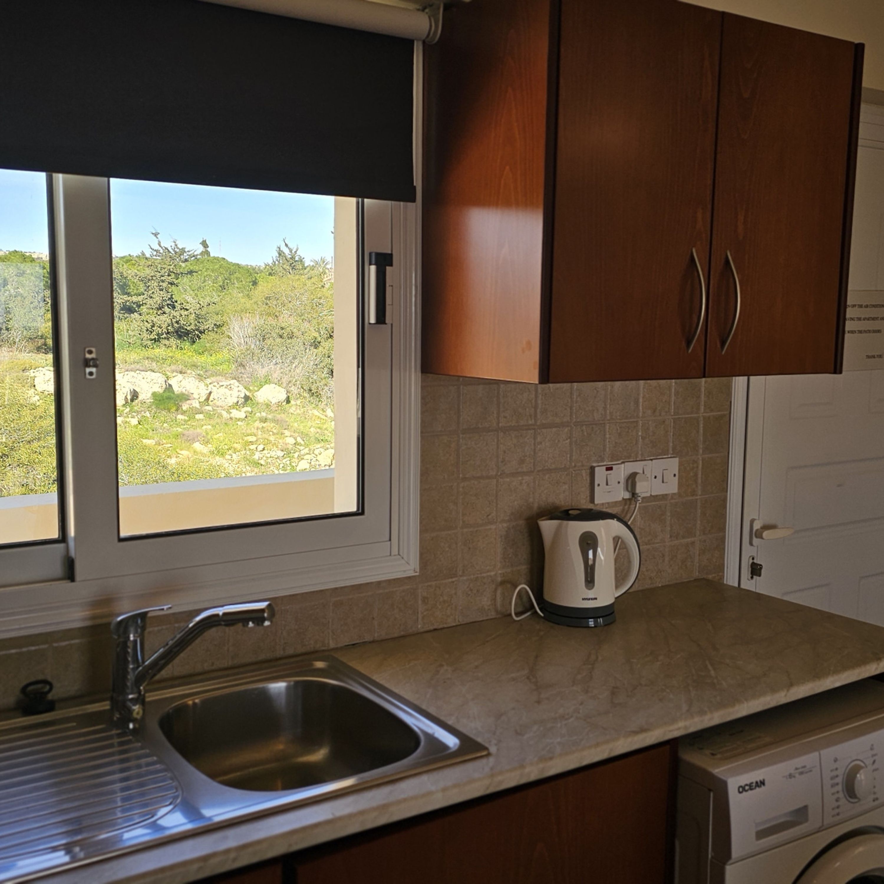 A kitchen with a sink, a kettle, and a washing machine.