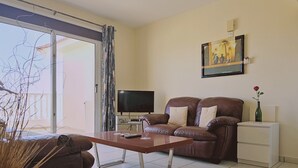 A living room with a sofa, a coffee table, a TV, and a painting on the wall. - 116 AN - Stay Nissi Blossom Apartment (Ayia Napa)