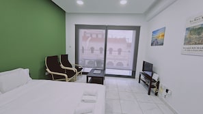A hotel room with a bed, a desk, a chair, a TV, and a window with a view of buildings. - 109 LIM 1 - Stay Olive Studio (Limassol)